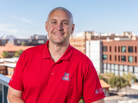 A photo of Denny Goforth who is on the Parent and Family Association Board, standing on a balcony with the Western Skyline behind him over looking the Unviersity of Arizona campus