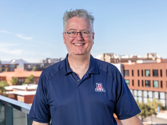 Scott McNamee standing on a balcony over looking the western skyline on the University of Arizona campus.