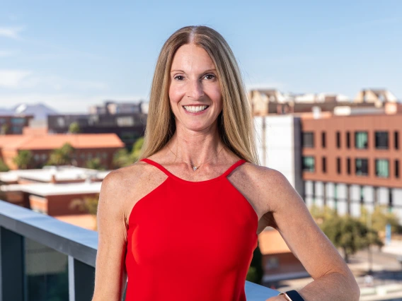 Parent & Family Association Board Member Gina Capizzi standing on a balcony with the western skyline behind her on the University of Arizona Campus