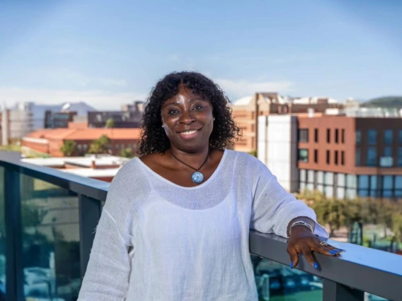 Parent and Family Association Board Member Bridget Akaeze is standing on a balcony with the western skyline behind her on the University of Arizona campus 