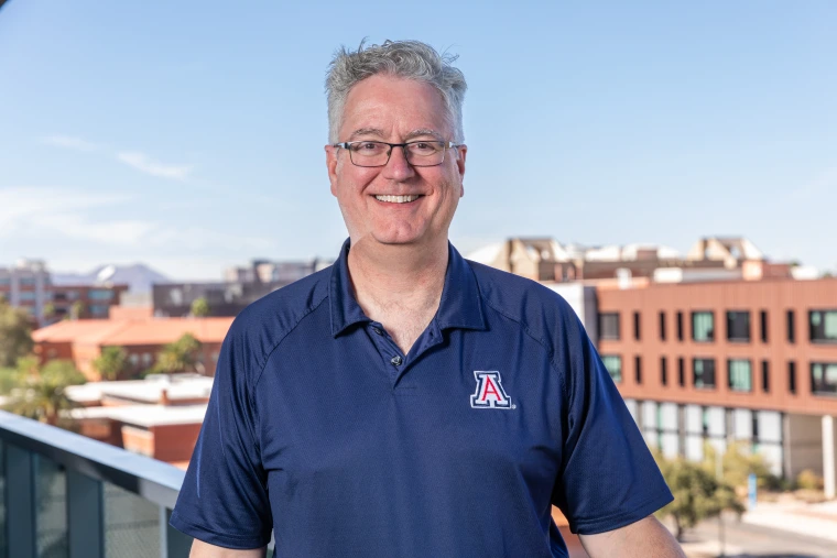 Scott McNamee standing on a balcony over looking the western skyline on the University of Arizona campus.