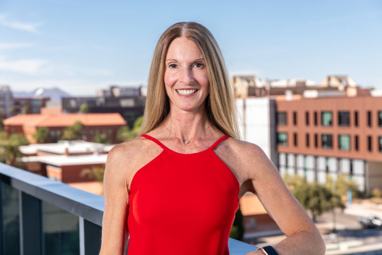 Parent & Family Association Board Member Gina Capizzi standing on a balcony with the western skyline behind her on the University of Arizona Campus