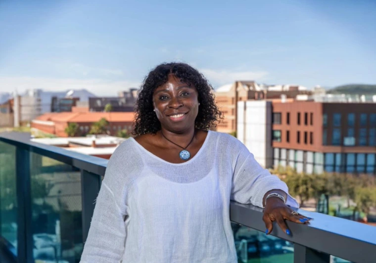 Parent and Family Association Board Member Bridget Akaeze is standing on a balcony with the western skyline behind her on the University of Arizona campus 